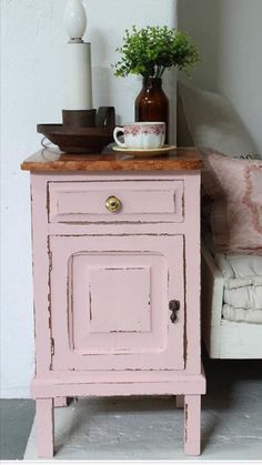 a small pink cabinet next to a white couch and table with flowers on the top