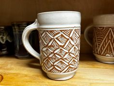 two coffee mugs sitting next to each other on a wooden shelf with cups in the background