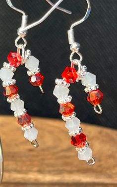 a pair of red, white and silver beaded earrings sitting on top of a wooden table