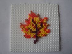 a red leaf made out of legos on top of a white surface with yellow and orange circles around it