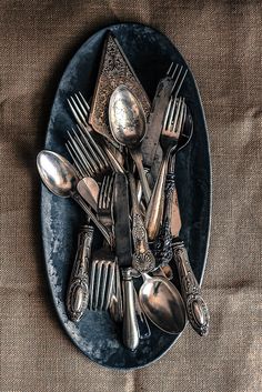 a plate with silverware and spoons on it sitting on a brown cloth covered tablecloth