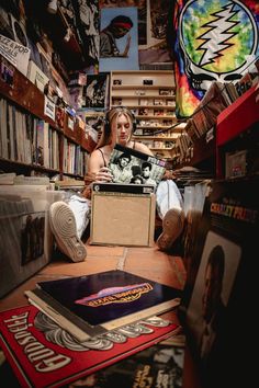 a woman is sitting on the floor with a box in her lap and surrounded by records