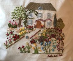 a hand embroidered house with flowers and trees in the front yard on a white sheet