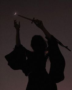 the silhouette of a woman holding an umbrella with her hands in the air at night