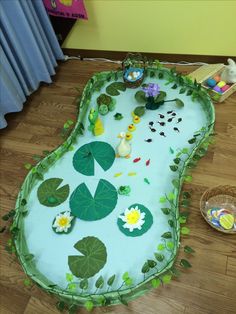 a cake shaped like a pond with lily pads and flowers on the bottom, sitting on top of a hard wood floor