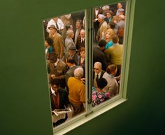 a group of people standing in front of a green wall looking out at the street