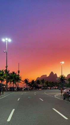 the sun is setting over mountains and palm trees in this city street with cars parked on the side