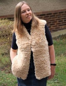 a woman standing in the grass wearing a furry vest