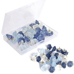 blue and white flowers are in a clear plastic container next to some other small buttons