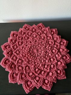 a pink crocheted doily sitting on top of a black table next to a white wall