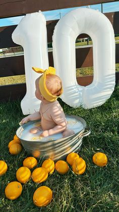 a baby sitting in a metal tub surrounded by oranges and large balloons that spell out the number 10