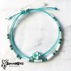 the bracelet is decorated with white beads and green glass beads on a turquoise string that has a heart shaped bead