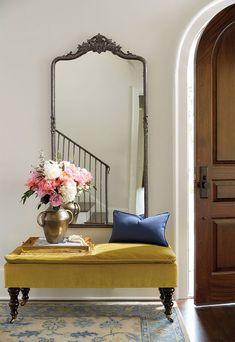 a yellow bench with flowers on it in front of a large mirror and stairs leading up to the second floor