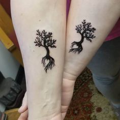 two people with tattoos on their arms holding each other's hands and one has a tree tattoo on it