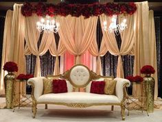 a white couch sitting under a chandelier in front of a red rose covered window