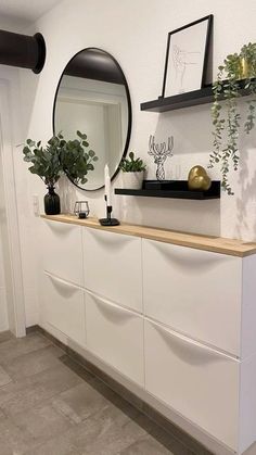 there is a mirror and some plants on the shelf in this room with white walls