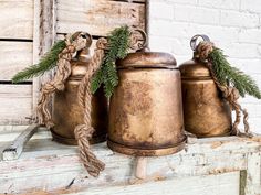 three metal bells with twine and pine needles on them sitting on a window sill