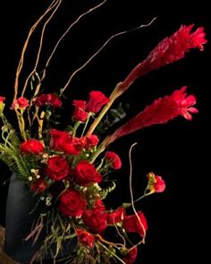 a vase filled with red flowers sitting on top of a wooden table next to a black wall