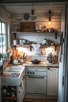 a small kitchen with white appliances and wooden flooring is lit by the light coming through the window