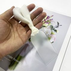 a hand holding a piece of white paper with flowers in the background