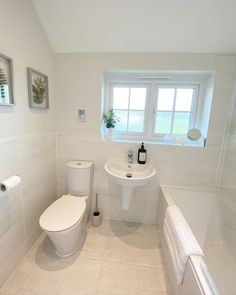 a white bathroom with a sink, toilet and bathtub next to a large window