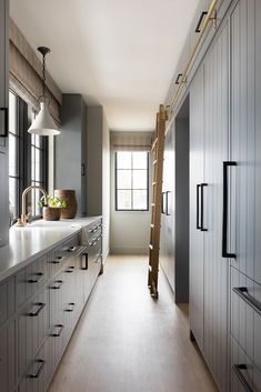 a long narrow kitchen with white cabinets and wood flooring, along with a ladder leading up to the window