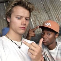 two young men standing next to each other with one pointing at the camera while the other points