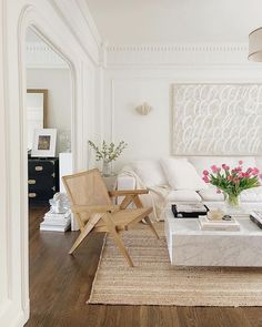 a living room filled with white furniture and flowers on top of a table in front of a mirror