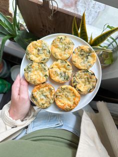 a person holding a plate with mini quiches on it and plants in the background