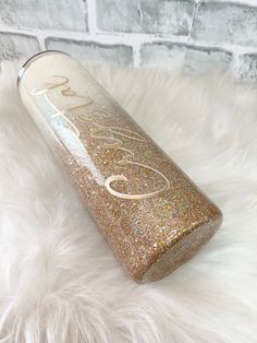 a gold glitter tumbler sitting on top of a white fur covered floor next to a brick wall