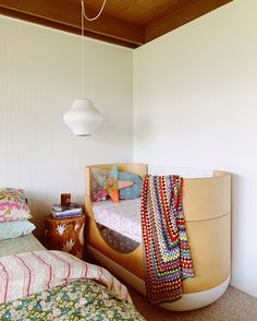 two beds in a room with white walls and wood ceilinging, one has a colorful blanket on the bed