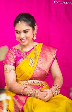 a woman in a yellow and pink sari sitting on a chair with her hands together