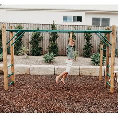 a young boy playing on a wooden swing set in his backyard with gravel and rocks