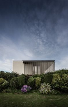 the house sits on top of a hill surrounded by bushes and flowers, with a dark sky in the background