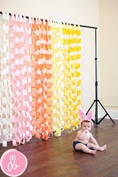 a baby sitting on the floor in front of a backdrop