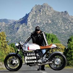 a man sitting on the back of a white and red motorcycle in front of mountains