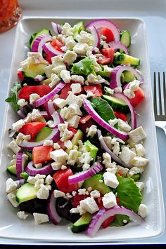 a white plate topped with a salad covered in feta cheese and red onion slices