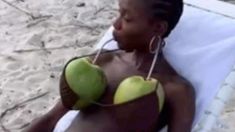 a woman laying on top of a beach next to a white towel and green fruit