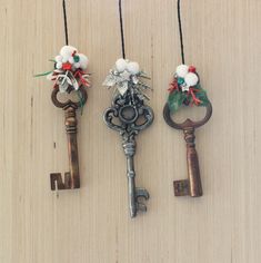 three old keys are hanging on the wall with some flowers and beads attached to them