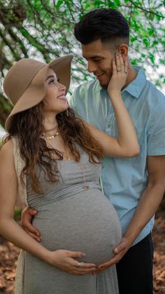 a pregnant woman standing next to a man wearing a hat and holding his hand on her belly