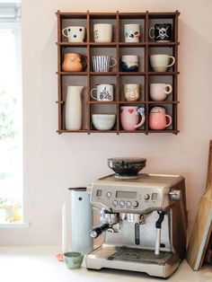 an espresso machine sitting on top of a counter next to a shelf filled with coffee cups