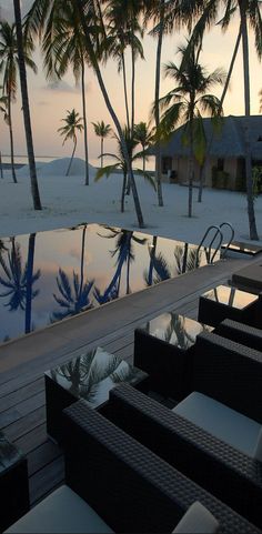 an empty pool surrounded by lounge chairs and palm trees on the beach at sunset or dawn