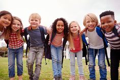 a group of young children standing next to each other in the grass with backpacks on