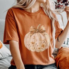 Fall Coquette Pumpkin with Bow Comfort Colors Shirt Embrace the cozy vibes of Fall with our Comfort Colors tee featuring a charming Coquette Pumpkin adorned with a delicate bow. The soft autumn hues of Yam, mustard, espresso, ivory, bay, and brick beautifully capture the essence of the season, making this shirt perfect for Fall, Halloween, and Thanksgiving celebrations. Crafted from 100% ring-spun US cotton, this Comfort Colors shirt offers a soft-washed, garment-dyed finish for an extra touch o Coquette Pumpkin, Fall Coquette, Floral Pumpkin, T Shirt Flowers, Autumn T Shirts, Soft Autumn, Baby Sweater, Pumpkin Shirt, Cozy Vibes