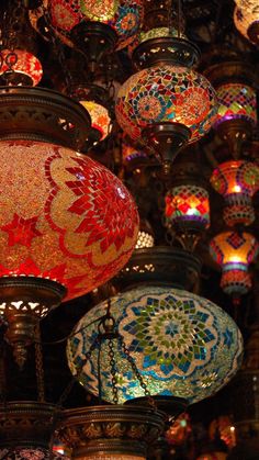 many colorful lights hanging from the ceiling in a room filled with other lamps and chandeliers