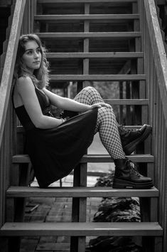 black and white photograph of a woman sitting on steps wearing fishnet stockings, tights and boots