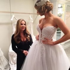 two women standing next to each other in front of wedding gowns on mannequins