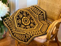 a crocheted blanket sitting on top of a chair next to a vase with flowers