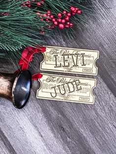 two christmas gift tags on top of a wooden table next to a pine tree with red ribbon