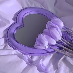 a purple heart shaped mirror sitting on top of a white bed covered in sheets and flowers